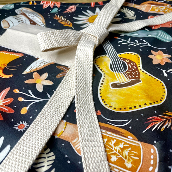 Amanda Bright Designs Delilah Apron with colorful western guitar cactus cowboy hat sunflower pattern on black background