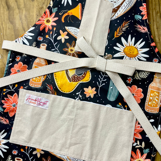 Amanda Bright Designs Desert Cowgirl Apron with colorful western guitar cactus cowboy hat sunflower pattern on black background