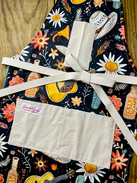 Amanda Bright Designs Desert Cowgirl Apron with colorful western guitar cactus cowboy hat sunflower pattern on black background