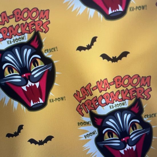 Pattern of 'Kat-Ka-Boom Firecrackers' logos on a yellow background with black bats from Black Cat Fireworks Amanda Bright Designs Couture Apron Collection