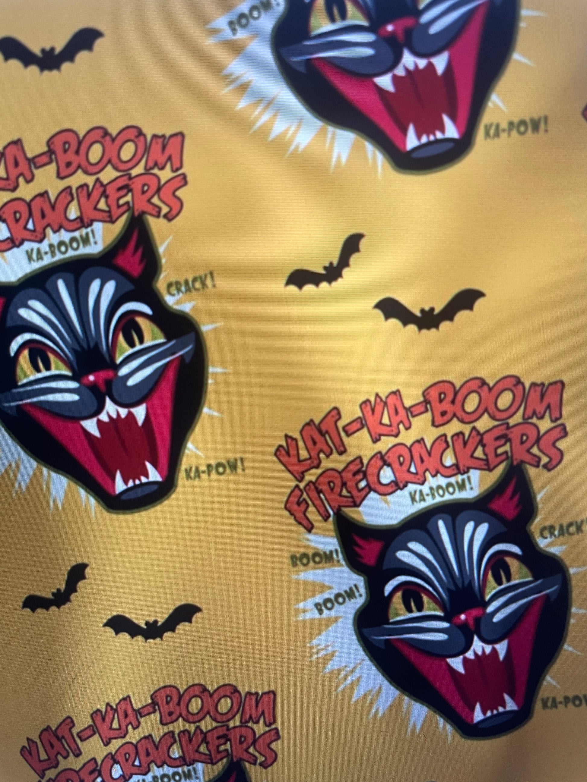 Pattern of 'Kat-Ka-Boom Firecrackers' logos on a yellow background with black bats from Black Cat Fireworks Amanda Bright Designs Couture Apron Collection