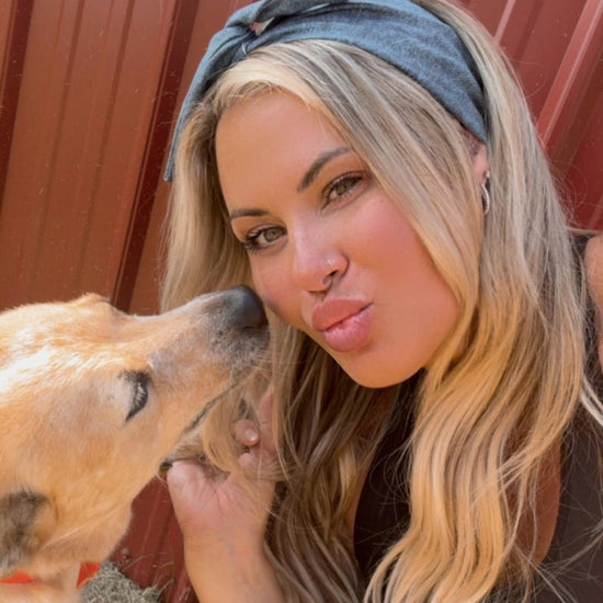 Woman with a dog kiss in an outdoor setting wearing medium wash denim original tie headband for women by Amanda Bright Designs