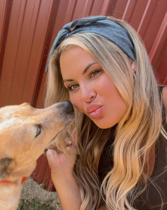 Woman with a dog kiss in an outdoor setting wearing medium wash denim original tie headband for women by Amanda Bright Designs