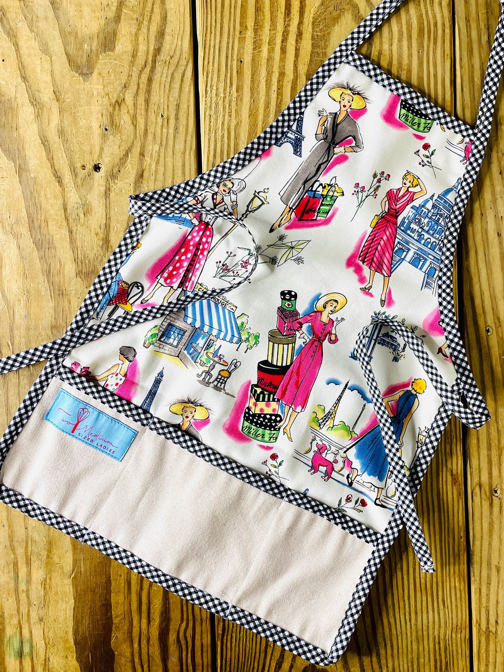 Amanda Bright Designs Children's apron with black gingham tie neck and multicolor design featuring retro fashion themes.
