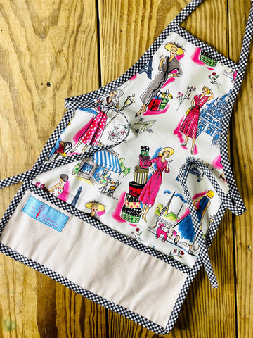 Amanda Bright Designs Children's apron with black gingham tie neck and multicolor design featuring retro fashion themes.